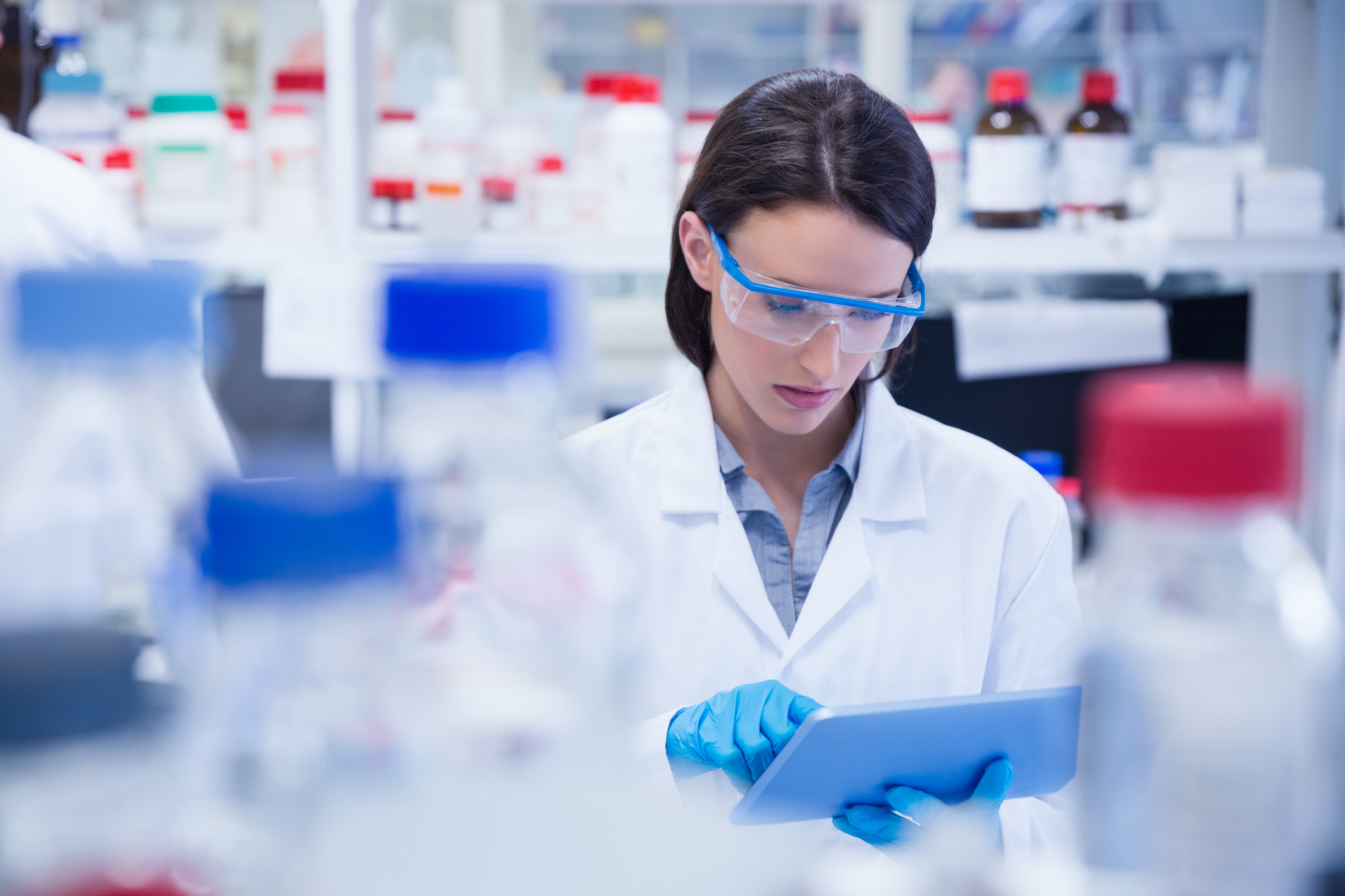 Laboratory researcher wearing safety glasses and reviewing a tablet