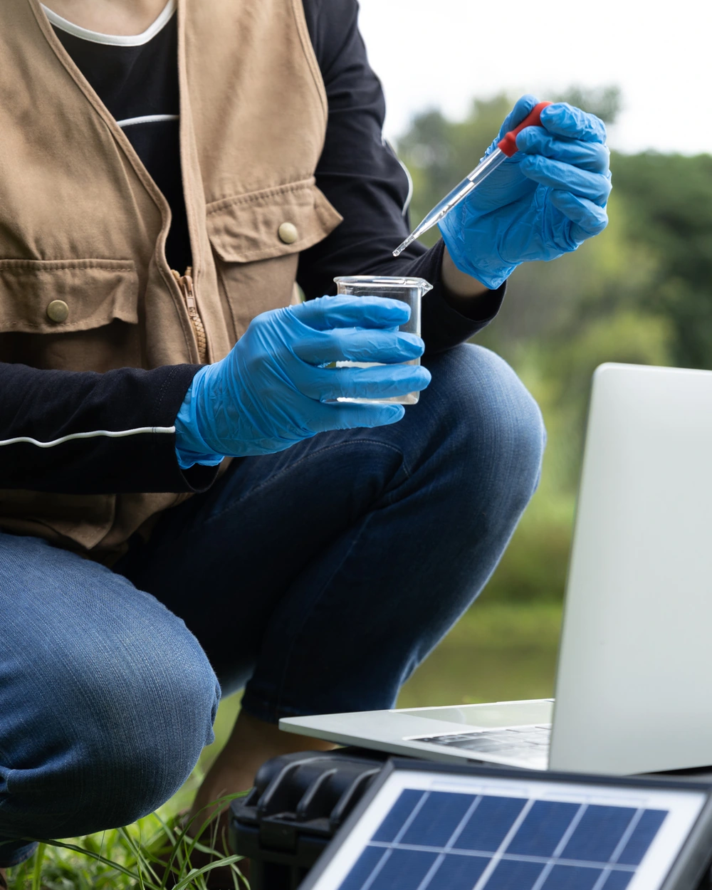 Researcher testing a water sample outdoors with a pipette beside a laptop