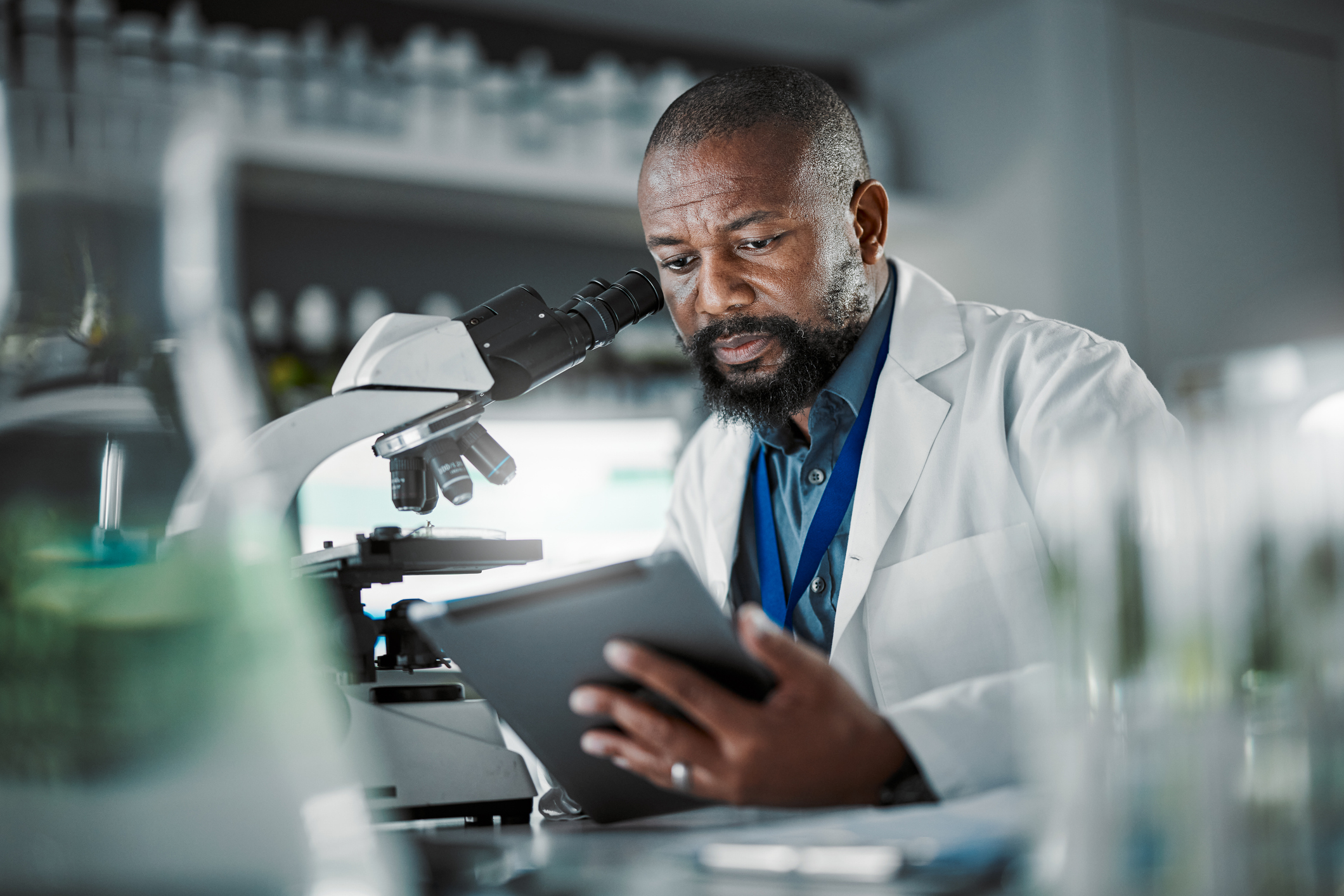 Laboratory researcher reviewing a tablet beside a microscope