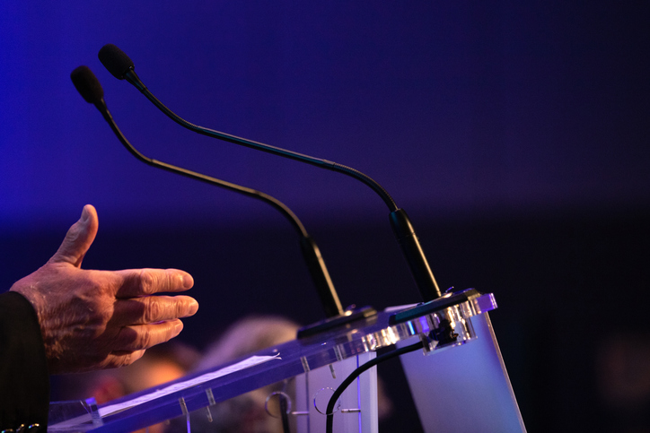 Microphones and a speaker’s hands at a lectern